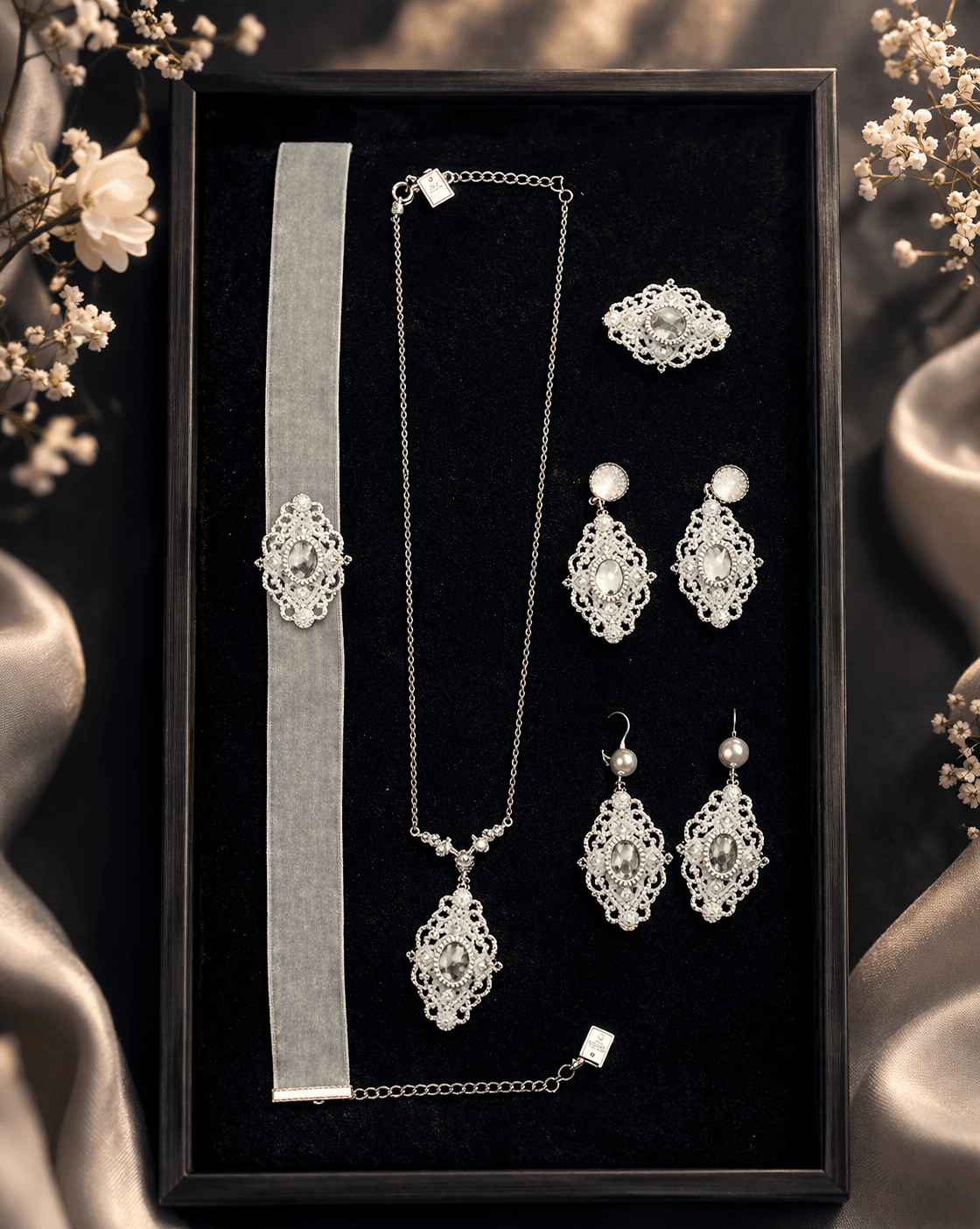 Filigranes silbernes Schmuckset mit Halskette, Ohrringen und Samt-Choker auf schwarzem Samt-Tablett mit zarten weißen Blüten.